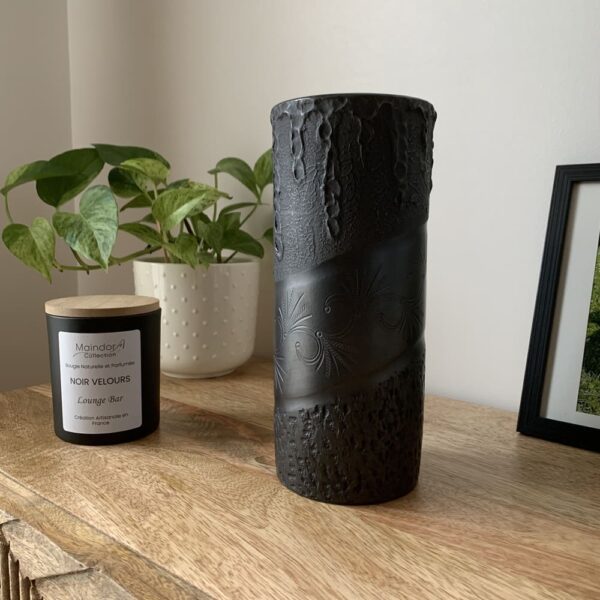 MaindorA-Vase noir artisanal en argile, fait main. Il est mis en valeur sur un meuble en bois pour une jolie décoration d'intérieur dans un mélange de bois et de noir. Ce vase noir Harmonia Secreta s'associe très bien avec la bougie parfumée Noir Velours.