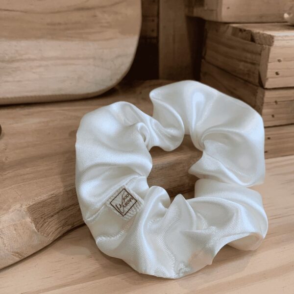 Maindora-Mon de petit Chouchou satiné dans sa couleur écru ou blanc cassé brillant. Le décor en bois naturel qui l'entoure met en valeur la pureté du chouchou Scrunchie