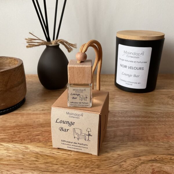 MaindorA-Belle mise en scène de la BOX de diffuseur de parfum de la senteur LOUNGE BAR. La fiole en verre et capuchon en bois carré est posé sur sar boite kraft sur un meuble en bois autour légèrement en arrière plan un peu flouté la grosse bougie NOIR VELOURS parfumée LOUNGE BAR, un vase d'ambiance Noir en céramique avec dedans des tiges en rotin noir et un pot en bois sur un socle de cuir noir. Cela confère une jolie atmosphère mystérieuse très cosy pour passer un bon moment entre amis.