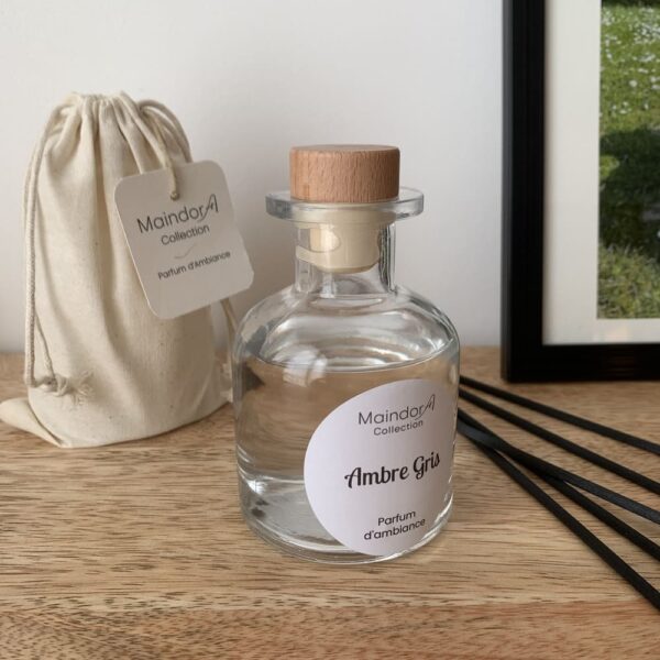 MaindorA-Le flacon APOTHICAIRE transparent du diffuseur de parfum d'intérieur est sur une console en bois de manguier. A coté le pochon d'emballage écru et les tiges de diffusion noires posées à coté.