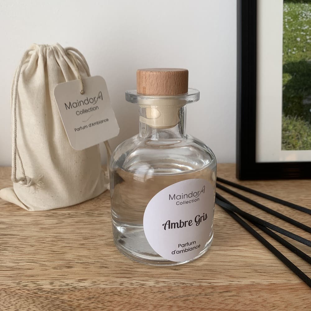 MaindorA-Le flacon APOTHICAIRE transparent du diffuseur de parfum d'intérieur est sur une console en bois de manguier. A coté le pochon d'emballage écru et les tiges de diffusion noires posées à coté.