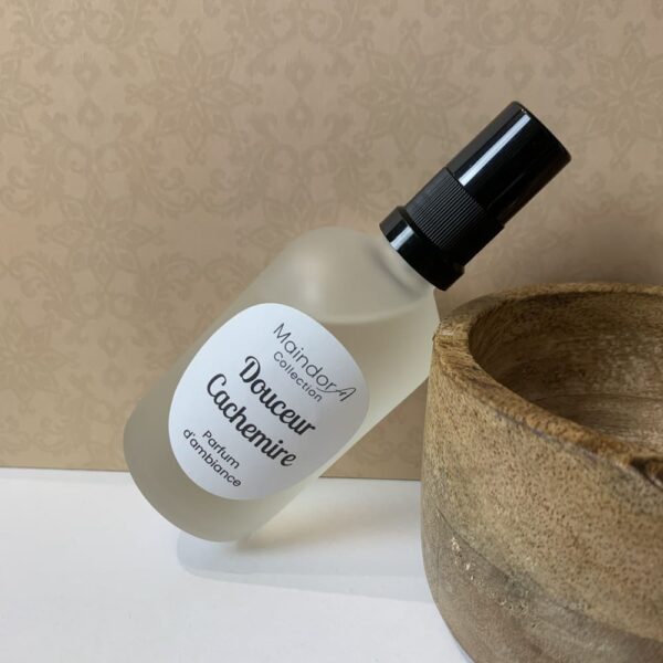 MaindorA-Douceur Cachemire voilà le nom de la fragrance indiquée sur l'étiquette ronde de ce spray parfum d'ambiance. Il est incliné et repose par un coin haut sur le bord d'un bol en bois artisanal.