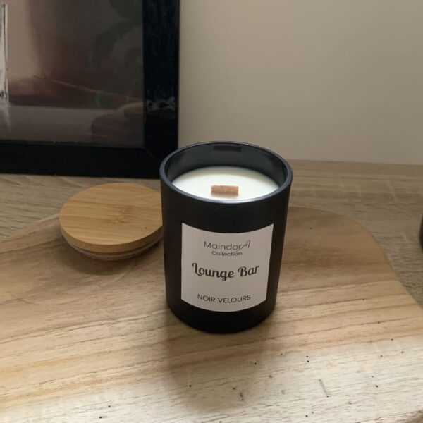 MaindorA-Bougie Parfumée 150 gr avec mèche en bois et cire végétale dans son verre noir. Cette bougie artisanale est posée sur un plateau en bois brut et s'intègre parfaitement à une décoration mélangeant le bois et des objets noirs. Ici un vase artisanal en poterie noire, à coté un cadre de contour noir apportent une harmonie naturelle, élégante et chic