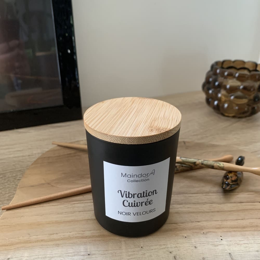 MaindorA-Bougie parfumée et naturelle aux notes boisées et épicées un peu masculines et puissantes. Cette bougie à la cire de soja et une mèche en bois est posée sur un meuble en bois dans une ambiance sobre et de méditation.