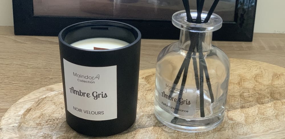 MaindorA-Le flacon APOTHICAIRE transparent du diffuseur de parfum d'intérieur est sur une console en bois de manguier. A coté le pochon d'emballage écru et les tiges de diffusion noires posées à coté.